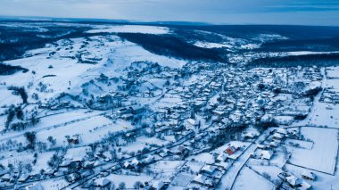 Kışın tarlalar ve ormanlar arasındaki hava manzaralı köy. Kış manzarası karla kaplı tarlalar ve kırsal kesimlerdeki ağaçlar.