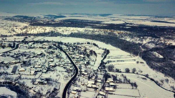 Luchtfoto dorp tussen de velden en bossen in de winter. winterlandschap besneeuwd veld en bomen op het platteland. — Stockfoto