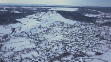 Kışın tarlalar ve ormanlar arasındaki hava manzaralı köy. Kış manzarası karla kaplı tarlalar ve kırsal kesimlerdeki ağaçlar.