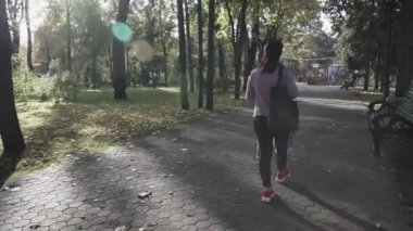 Genç bir kadın sonbahar parkında yürüyor. Kız güneşli bir günde sonbahar şehir parkında yürüyor. Düşen sarı ve turuncu yapraklar
