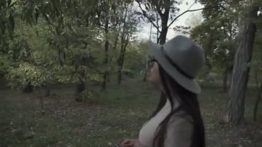 Sonbahar parkında şapkalı ve gözlüklü genç bir esmer yürüyor.