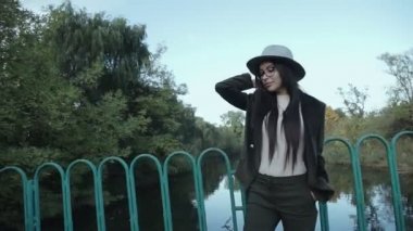Duygusal açıdan mutlu, uzun saçlı, şapkalı ve kameraya gülümseyen esmer kadını yakından çek. Kuaförden sonra mükemmel makyajlı, parkta poz veren güzel bir model. Moda ve güzellik kavramı.