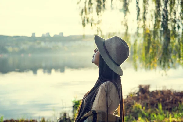 Närbild av glad känslomässigt brunett kvinna med långt hår och hatt, ler mot kameran. Vacker modell med perfekt makeup efter salong, poserar i parken. Begreppet mode och skönhet. — Stockfoto