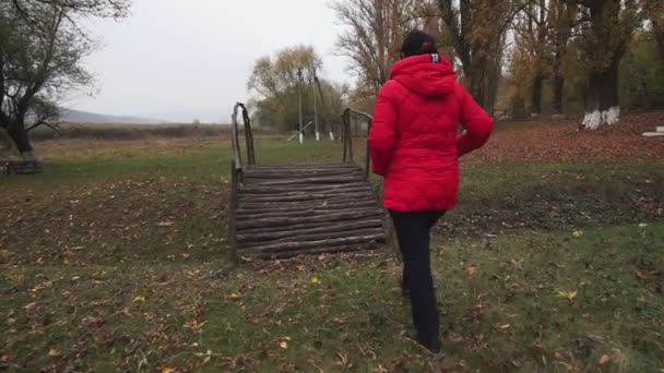 Uma Mulher Uma Jaqueta Vermelha Caminha Uma Ponte Madeira Parque — Vídeo de Stock