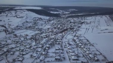 Kışın tarlalar ve ormanlar arasındaki hava manzaralı köy. Kış manzarası karla kaplı tarlalar ve kırsal kesimlerdeki ağaçlar.