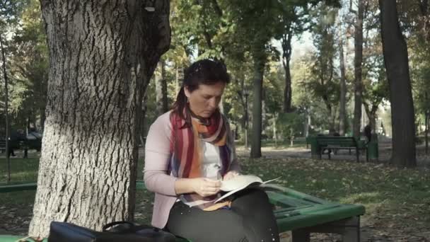 Sonbaharda Bankta Otururken Ilginç Bir Kitap Okuyan Eğlenen Bir Kadın — Stok video