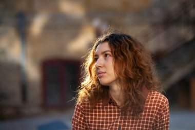 Olağanüstü kıvırcık kızıl saçlı genç bir kadın şehir merkezindeki sokakta kameraya bakıyor. Kadın portresi.