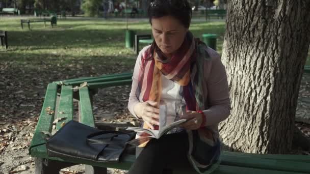 Kobieta Czytająca Ciesząca Się Ciekawą Książką Siedząc Jesienią Ławce Zamknij — Wideo stockowe