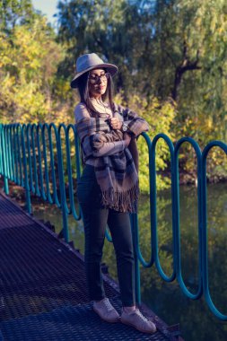 Duygusal açıdan mutlu, uzun saçlı, şapkalı ve kameraya gülümseyen esmer kadını yakından çek. Kuaförden sonra mükemmel makyajlı, parkta poz veren güzel bir model. Moda ve güzellik kavramı.