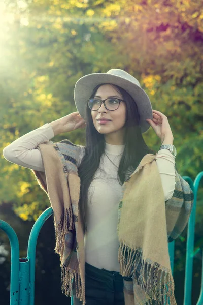 Gros plan de heureuse femme brune émotionnellement avec les cheveux longs et des lunettes dans le chapeau. Beau modèle avec un maquillage parfait après salon, posant dans le parc. Concept de mode et de beauté . — Photo