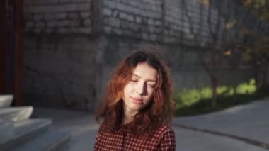 Olağanüstü kıvırcık kızıl saçlı genç bir kadın şehir merkezindeki sokakta kameraya bakıyor. Kadın portresi.