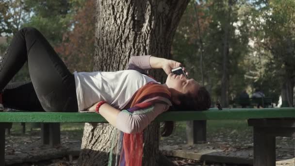 Dziewczyna Rozmawia Przez Telefon Leżąc Ławce Parku — Wideo stockowe