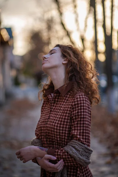 Sonhando jovem mulher com cabelo encaracolado gengibre vermelho espetacular olhando para câmera posando ao ar livre no centro da rua. Retrato feminino . — Fotografia de Stock
