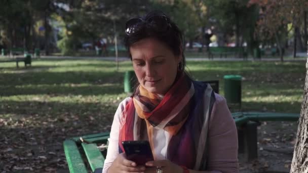 Νεαρή Γυναίκα Γράφει Μηνύματα Ενώ Κάθεται Ένα Παγκάκι Στο Πάρκο — Αρχείο Βίντεο