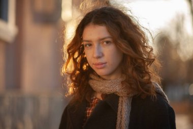 Olağanüstü kıvırcık kızıl saçlı genç bir kadın şehir merkezindeki sokakta kameraya bakıyor. Kadın portresi.