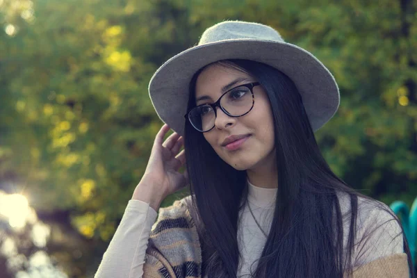 Primer plano de feliz mujer morena emocionalmente con el pelo largo y sombrero, sonriendo a la cámara. Hermosa modelo con maquillaje perfecto después del salón, posando en el parque. Concepto de moda y belleza . —  Fotos de Stock