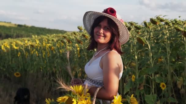 帽子を被った女性と白いドレスがひまわり畑を歩いている — ストック動画