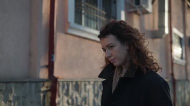 Olağanüstü kıvırcık kızıl saçlı genç bir kadın şehir merkezindeki sokakta kameraya bakıyor. Kadın portresi.
