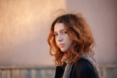 Olağanüstü kıvırcık kızıl saçlı genç bir kadın şehir merkezindeki sokakta kameraya bakıyor. Kadın portresi.