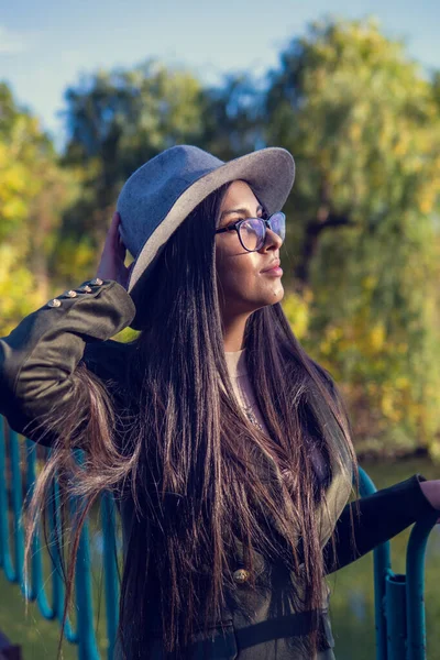 Close up de mulher feliz emocionalmente morena com cabelo longo e chapéu, sorrindo para a câmera. Modelo bonito com maquiagem perfeita após o salão, posando no parque. Conceito de moda e beleza . — Fotografia de Stock