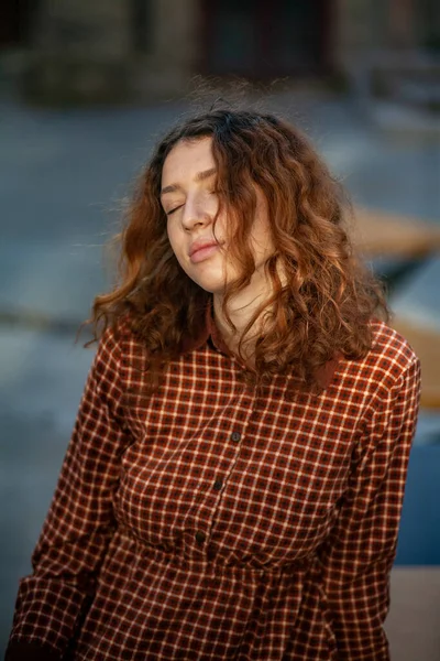 Sonhando jovem mulher com cabelo encaracolado gengibre vermelho espetacular olhando para câmera posando ao ar livre no centro da rua. Retrato feminino . — Fotografia de Stock