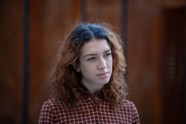 Olağanüstü kıvırcık kızıl saçlı genç bir kadın şehir merkezindeki sokakta kameraya bakıyor. Kadın portresi.