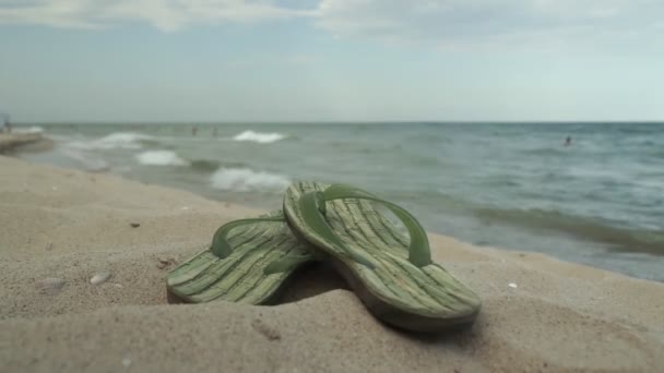 砂の上に横たわるビーチのためのアクセサリー ビーチの砂の上に男性用スリッパとサングラス — ストック動画