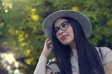 Duygusal açıdan mutlu, uzun saçlı, şapkalı ve kameraya gülümseyen esmer kadını yakından çek. Kuaförden sonra mükemmel makyajlı, parkta poz veren güzel bir model. Moda ve güzellik kavramı.