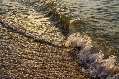 Güneşin doğuşunda kumlu sahilde denizin yumuşak dalgası