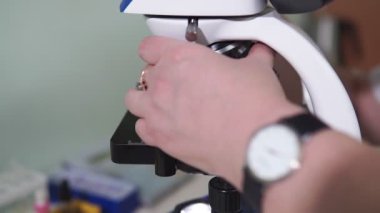 Kadın araştırmacı bilim adamı mikroskop altında biyolojik örneklere bakıyor. O ve meslektaşları büyük bir modern laboratuvar tıp merkezinde çalışıyorlar..