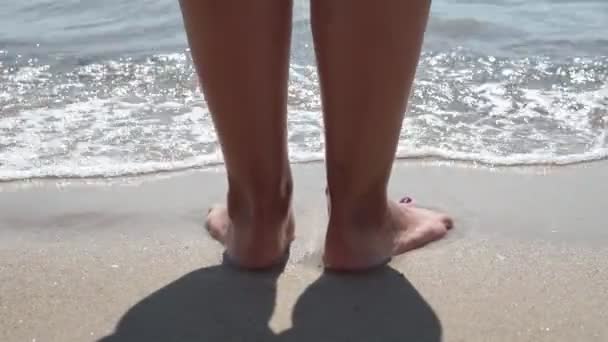 Ondas marinas lavando sobre pies femeninos bronceados. Hermosa joven que se relaja en la costa durante las vacaciones de verano. Piernas de niña acostada en la playa en un día soleado. De cerca. . — Vídeos de Stock