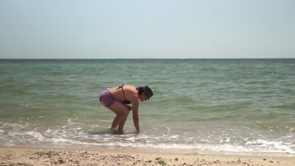 Uma mulher bronzeada está de pé de costas para o mar, olhando para o mar . — Vídeo de Stock