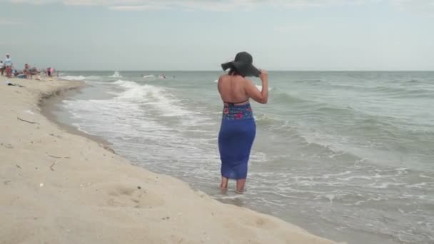 海のそばのビーチで帽子と青いドレスの女性 — ストック動画