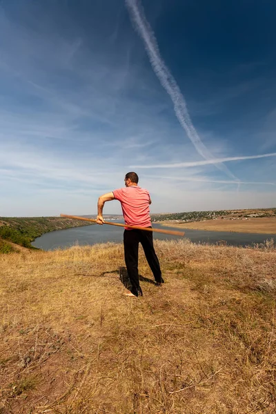 Um homem está envolvido em ginástica curativa com um pólo na natureza. Estilo de vida saudável . — Fotografia de Stock