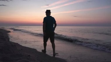 Gün doğumunda ıssız bir sahilde huzur içinde yürüyen bir adam silueti. deniz manzarası