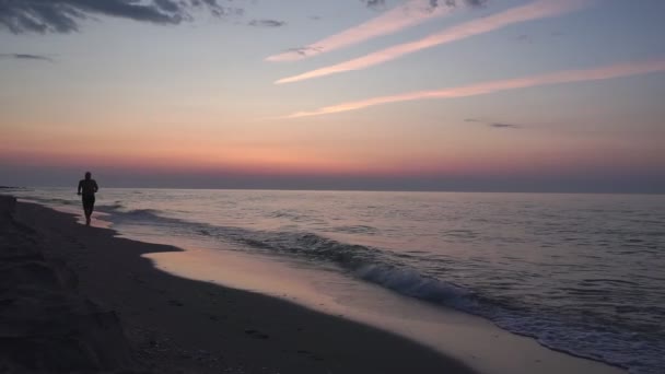 日の出に無人のビーチを平和的に歩く男のシルエット — ストック動画