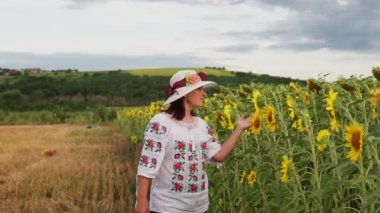 Şapkalı genç bir kadın uzun ayçiçekleri ile tarlada yürüyor. Dikey görünüm.