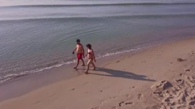 Sunset 'te erkek ve kadın sahilde yürüyor, tatilde çiftlerin kumsalda eğlenirken çekilmiş görüntülerini izliyorlar. Gün batımında kumsalda yürüyen çift..