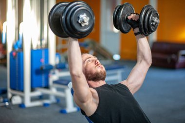 Spor kulübünde ağırlık kaldıran güçlü adam. Spor salonunda dambıllarla kaslarını çalıştıran yakın çekim adam. Yakışıklı fitness eğitmeni fitness merkezinde güç kaldırma egzersizleri yapıyor.