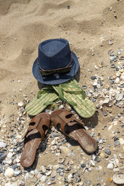 Accessoires voor het strand liggend op het zand, heren slippers en — Stockfoto