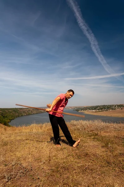 A man is engaged in curative gymnastics with a pole on the nature. Healthy lifestyle. — Stock Photo, Image