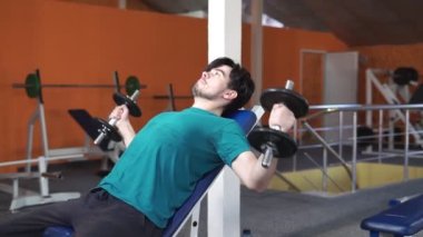 Spor kulübünde ağırlık kaldıran güçlü adam. Spor salonunda dambıllarla kaslarını çalıştıran yakın çekim adam. Yakışıklı fitness eğitmeni fitness merkezinde güç kaldırma egzersizleri yapıyor.