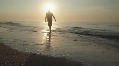 Gün doğumunda ıssız bir sahilde huzur içinde yürüyen bir adam silueti. deniz manzarası