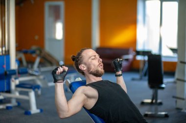 Spor kulübünde ağırlık kaldıran güçlü adam. Spor salonunda dambıllarla kaslarını çalıştıran yakın çekim adam. Yakışıklı fitness eğitmeni fitness merkezinde güç kaldırma egzersizleri yapıyor.