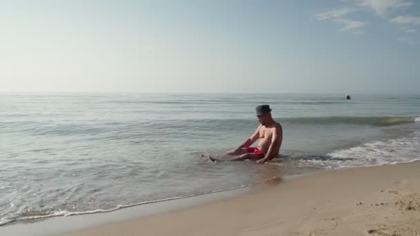 ショートパンツの大人の男がビーチに座っている — ストック動画