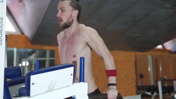 Ein junger athletischer Mann übt körperliche Arbeit in der Turnhalle aus und schüttelt die Muskeln der Hände mit Hilfe eines Trainingsgeräts, eines Trainers in der Turnhalle, eines gesunden Lebensstils, eines Rückens — Stockvideo