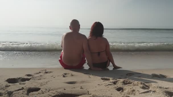 Bir adam ve bir kadın sahilde oturur ve denizin tadını çıkarırlar. — Stok video