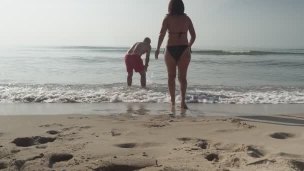 男と女が手を取り合って水の中に入る。海による素晴らしい休暇. — ストック動画