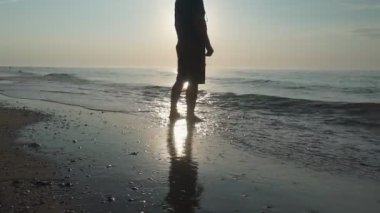 Gün doğumunda ıssız bir sahilde huzur içinde yürüyen bir adam silueti. deniz manzarası