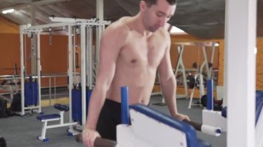 Genç bir atletik adam spor salonunda fiziksel emek harcıyor, egzersiz makinesinin, spor salonundaki antrenörün, sağlıklı bir yaşam tarzının ve sırtının yardımıyla ellerinin kaslarını sıkıyor.